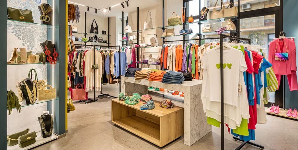 Scatto panoramico negozio abbigliamento donna con strutture soffitto-pavimento, gondole centrali e tavoli espositivi. Spettacolo Design